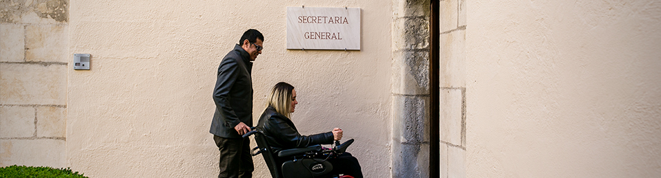 Hombre con mujer en silla de ruedas accediendo a través de una rampa de acceso a Secretaría General en patio del Hospital Real